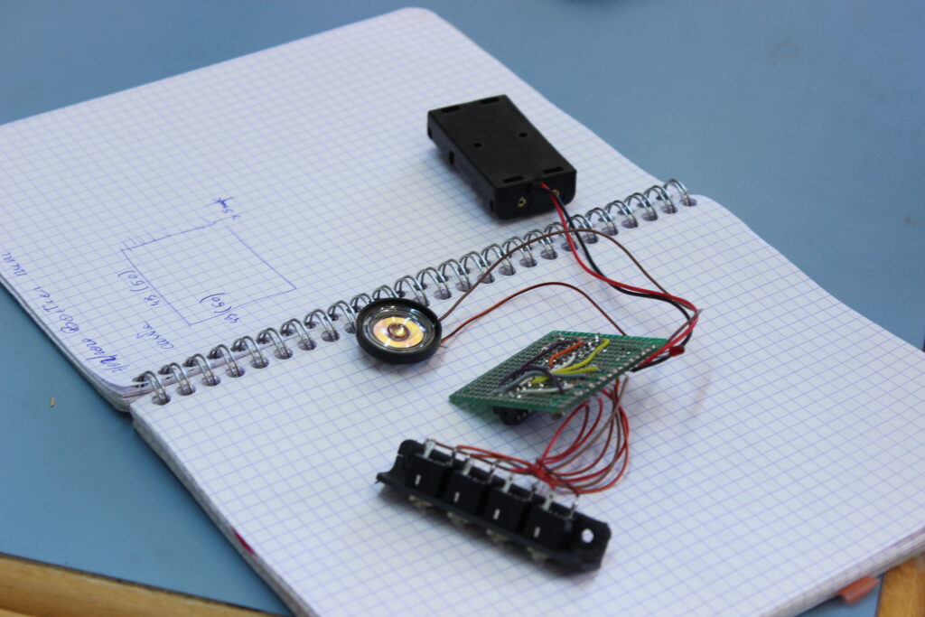 Un cahier de brouillon ouvert sur lequel sont notées des mesures. Dessus est posé un prototype de circuit électrique.